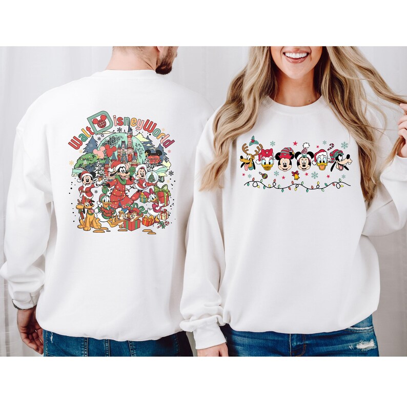 Op de afbeelding: Witte sweatshirts met feestelijke Disney-personages. E&eacute;n sweatshirt toont Mickey Mouse, Minnie Mouse en vrienden met de tekst "Walt Disney World". De andere heeft Disney-personages met kerstverlichting en feestelijke hoeden.