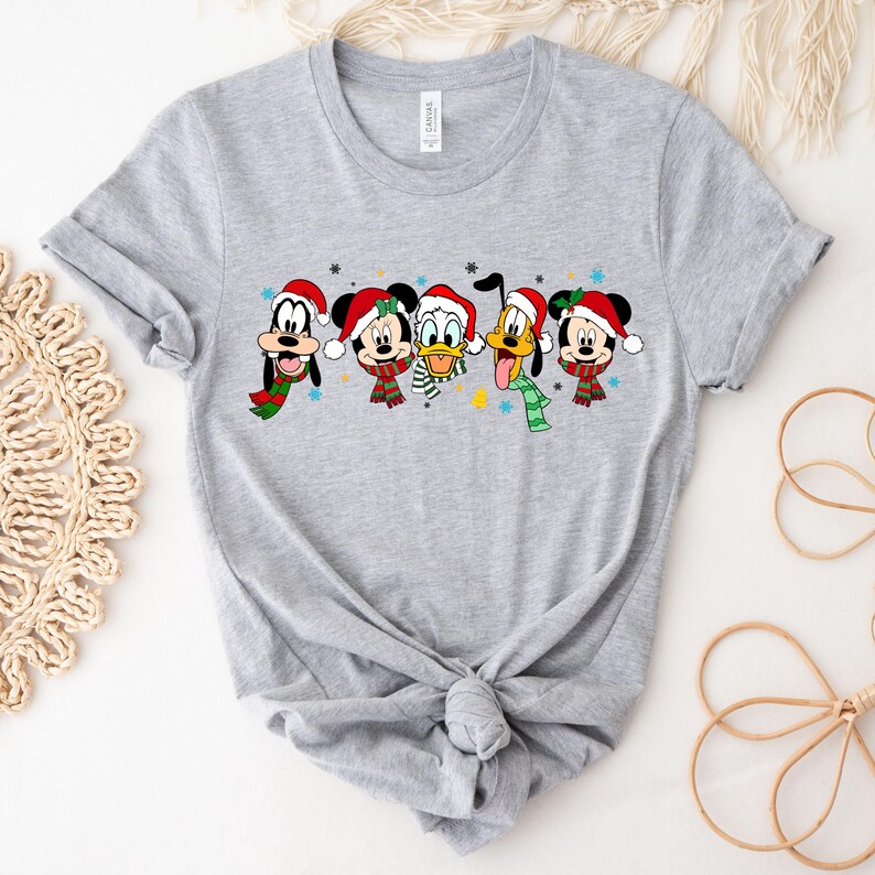 May include: A gray t-shirt with a Christmas-themed design featuring Mickey Mouse, Minnie Mouse, Donald Duck, Goofy, and Pluto wearing Santa hats and scarves.