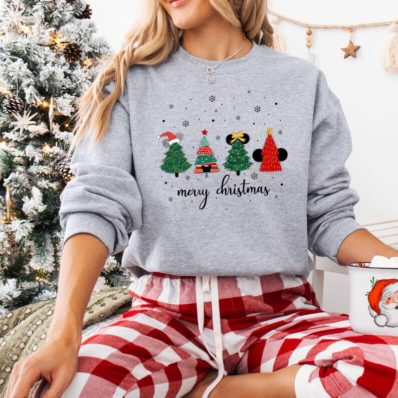 May include: A gray sweatshirt with a festive Christmas tree design. The trees are decorated with Santa hats, bows, and Mickey Mouse ears. The words "merry christmas" are written in a script font below the trees.