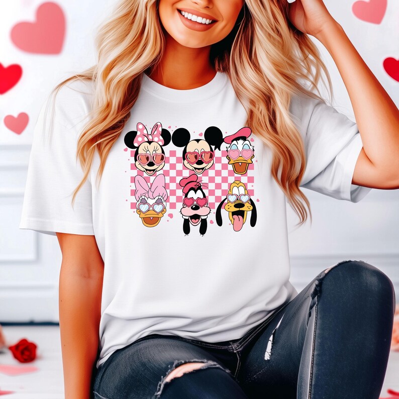 May include: White t-shirt with a pink and white checkered background featuring cartoon characters from Disney's Mickey Mouse franchise wearing heart-shaped sunglasses. The characters include Mickey Mouse, Minnie Mouse, Donald Duck, Goofy, and Pluto.