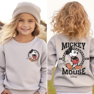 May include: A gray sweatshirt with a Mickey Mouse graphic on the front and "MICKEY MOUSE 1928" text on the back. The Mickey Mouse graphic is in a circle with a checkered pattern.