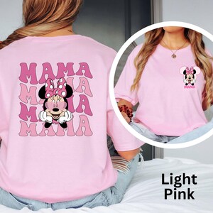 Puede incluir: Camiseta rosa claro con un dise&ntilde;o de Minnie Mouse y la palabra "MAMA" en una fuente retro. El dise&ntilde;o se repite en la parte posterior. La camiseta es de color rosa claro.