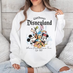 May include: White sweatshirt featuring the text "Walt Disney's Disneyland" in black script above a graphic of Mickey Mouse, Minnie Mouse, Donald Duck, Daisy Duck, Goofy, and Pluto. The text "Where Dreams Come True Est. 1955" is below the graphic.