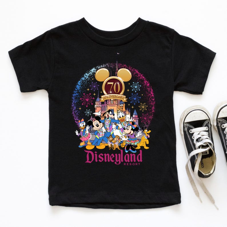 Op de afbeelding: Zwart T-shirt met een kleurrijke afbeelding van Mickey Mouse en zijn vrienden die het 70-jarig jubileum van Disneyland vieren. De afbeelding bevat vuurwerk, het Disneyland-kasteel en de tekst "Disneyland Resort".