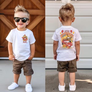 Puede incluir: Una camiseta blanca con un coche de dibujos animados rojo y el texto "It's my birthday" en la espalda. La parte delantera de la camiseta tiene un coche de dibujos animados m&aacute;s peque&ntilde;o y el nombre "Alex". El ni&ntilde;o lleva pantalones cortos marrones y zapatillas blancas.