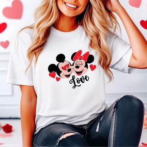 May include: White t-shirt with a graphic of Mickey Mouse and Minnie Mouse kissing with red hearts and the word "Love" printed below.
