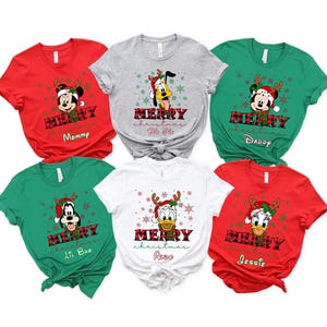 May include: Six red, green, white, and gray t-shirts with a Christmas theme. Each shirt features a different Disney character, including Mickey Mouse, Pluto, and Donald Duck. The shirts have the text "Merry Christmas" and a personalized name on each shirt.