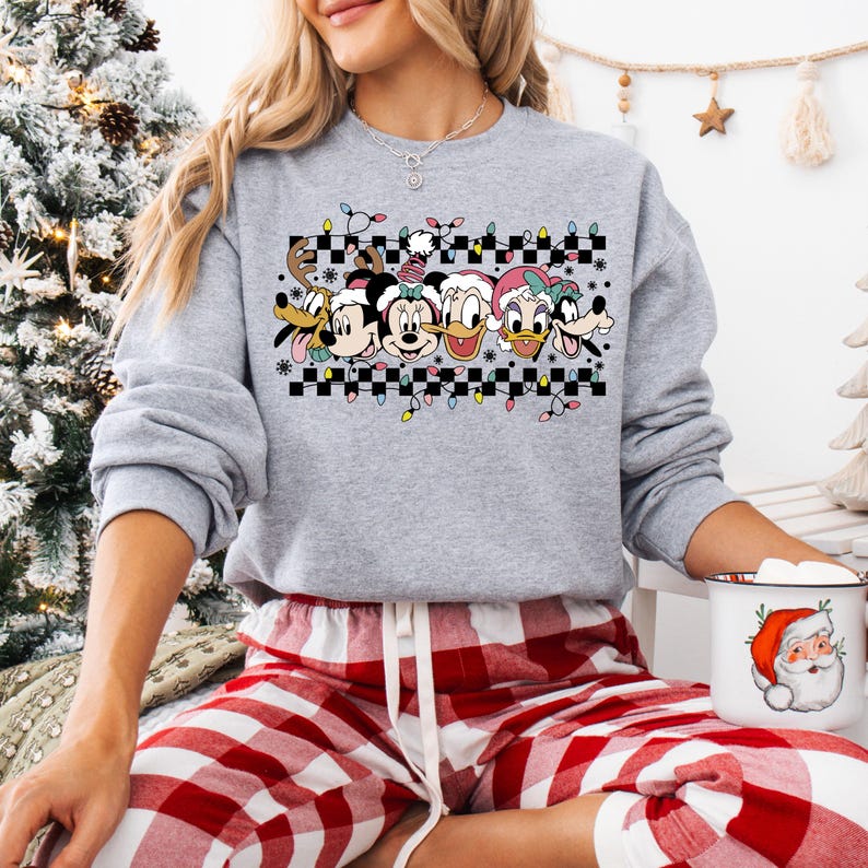 May include: A gray sweatshirt with a checkered pattern and a row of Disney characters wearing Santa hats. The characters include Mickey Mouse, Minnie Mouse, Donald Duck, Daisy Duck, and Pluto. The sweatshirt has a festive Christmas theme.