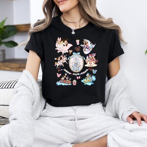 May include: Black t-shirt featuring a colorful graphic of various Disney characters and icons. The design includes images of Minnie and Mickey Mouse, a castle, and other themed elements. The shirt is a classic crew neck style.