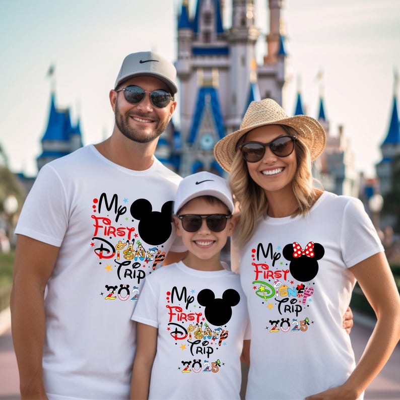 Peut inclure: Trois personnes portant des t-shirts blancs avec un motif Mickey Mouse et le texte "My First Disney Trip 2023". Les chemises ont des graphiques color&eacute;s et une silhouette noire de Mickey Mouse. La famille sourit devant un ch&acirc;teau.