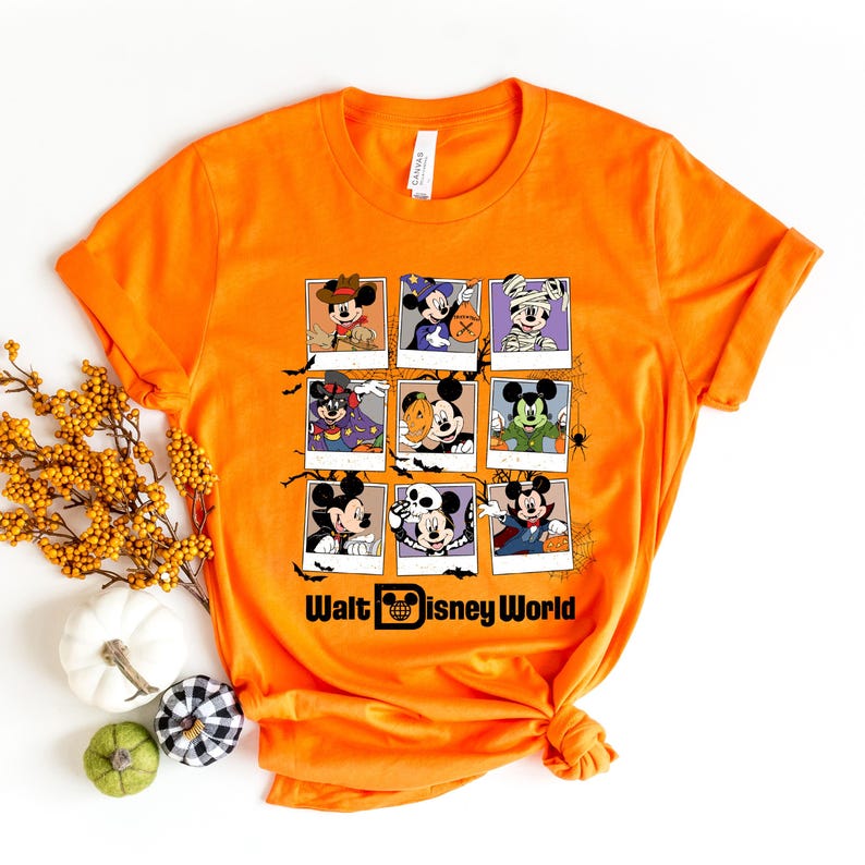 Op de afbeelding: Oranje T-shirt met een afbeelding van Mickey Mouse en zijn vrienden verkleed in Halloween-kostuums. De afbeelding is in een raster van negen vierkanten gerangschikt. De tekst "Walt Disney World" staat onderaan de afbeelding.