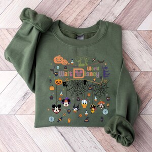 May include: Green sweatshirt with a Halloween-themed design featuring Mickey Mouse and other Disney characters. The design includes a banner that says "Walt Disney World" and various Halloween icons like pumpkins, bats, and spiderwebs.