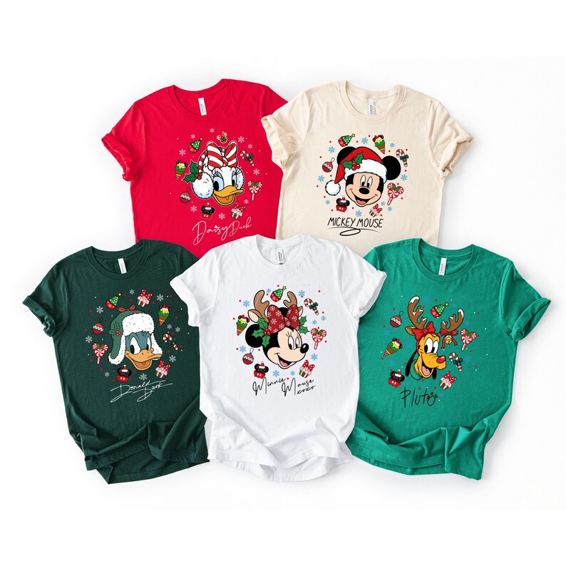 May include: A collection of Christmas-themed t-shirts featuring Disney characters. Designs include Mickey Mouse, Minnie Mouse, Donald Duck, and Pluto, each adorned with festive holiday elements like Santa hats, reindeer antlers, and candy canes. The shirts come in various colors.