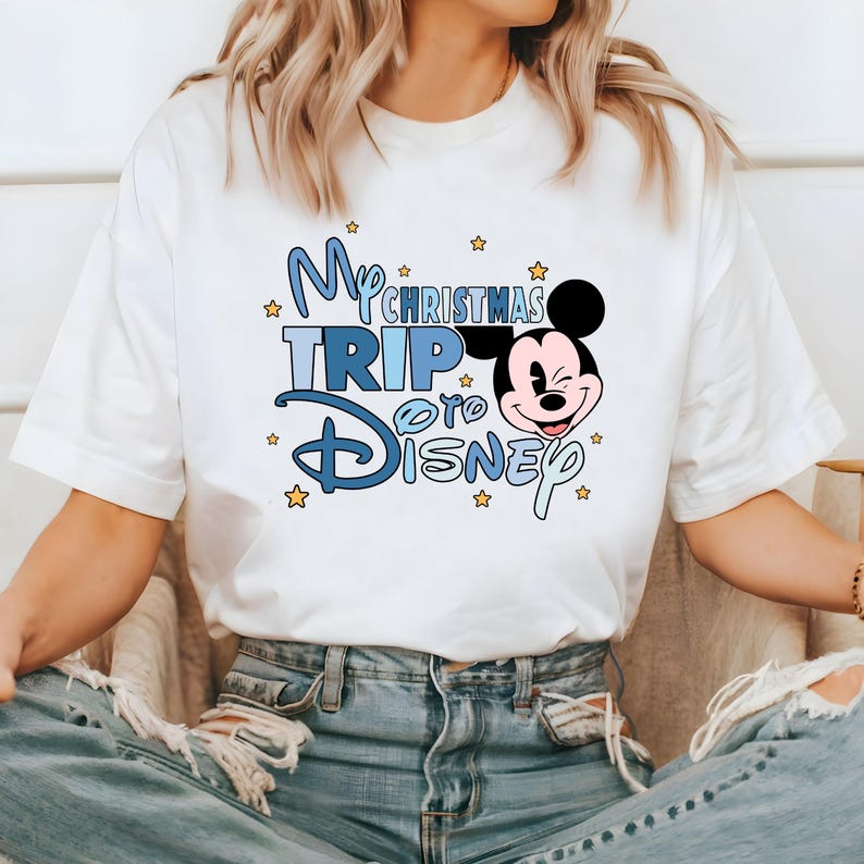 Puede incluir: Camiseta blanca con un gr&aacute;fico azul y blanco que dice "My Christmas Trip to Disney" con una imagen de dibujos animados de Mickey Mouse.