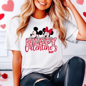 May include: White t-shirt with a pink and red heart pattern. Mickey Mouse and Minnie Mouse are peeking over the text "Happy Valentine's Day".
