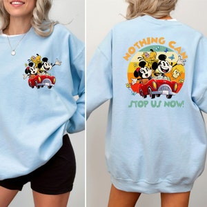 May include: Light blue sweatshirt with a vintage-style graphic of Mickey Mouse, Minnie Mouse, and Pluto driving a red car. The text "Nothing Can Stop Us Now!" is printed on the back of the sweatshirt.