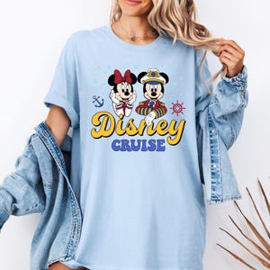 May include: Light blue t-shirt with a graphic of Mickey Mouse and Minnie Mouse dressed as a captain and a sailor. The text "Disney Cruise" is printed in yellow on the shirt.