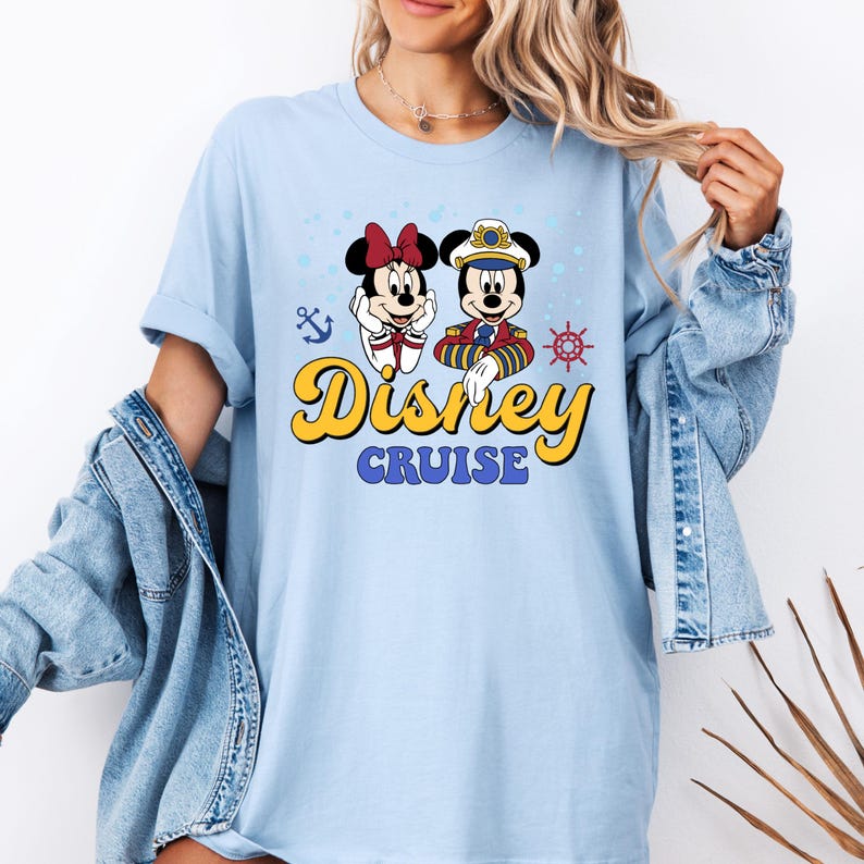 May include: Light blue t-shirt with a graphic of Mickey Mouse and Minnie Mouse dressed as a captain and a sailor. The text "Disney Cruise" is printed in yellow on the shirt.