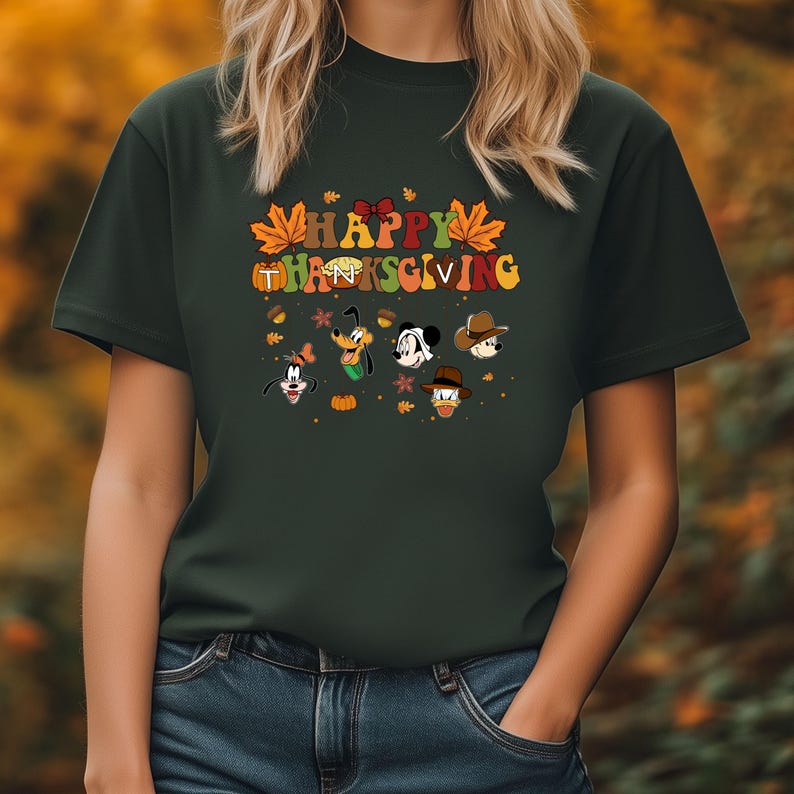 Op de afbeelding: Donkergroen t-shirt met de woorden "HAPPY THANKSGIVING" in kleurrijke letters en herfstthema graphics. Met gezichten van stripfiguren zoals Mickey Mouse, Donald Duck en Goofy. Een feestelijk en leuk ontwerp.