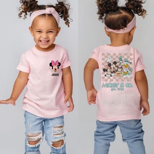 May include: Pink short-sleeved t-shirt with a Mickey Mouse and friends graphic on the back and a Minnie Mouse graphic on the front. The shirt says "Mickey & Co. Est. 1928" on the back and "Jessie" on the front.