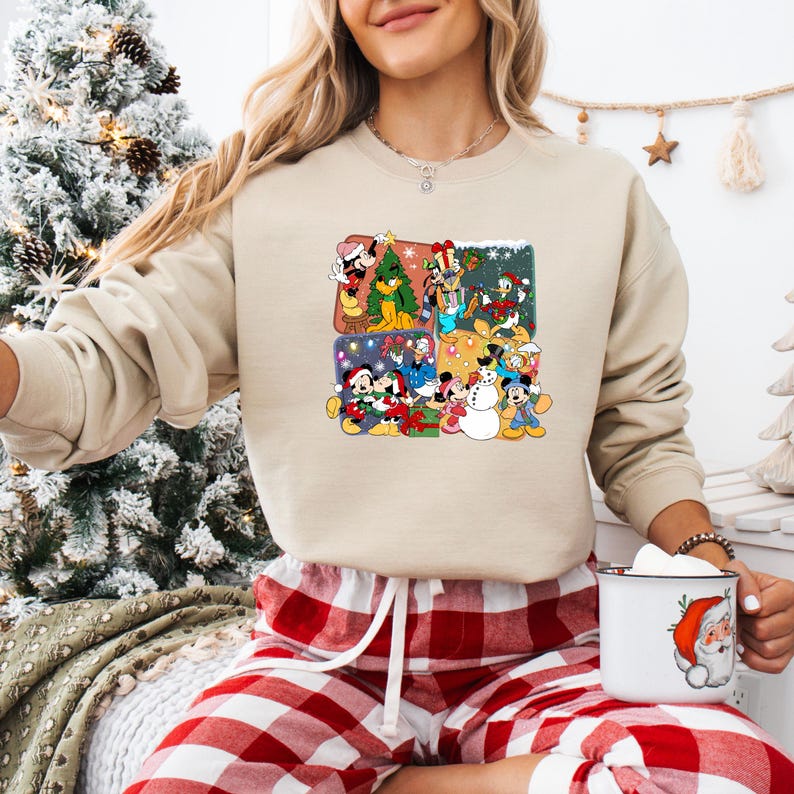 May include: Beige crewneck sweatshirt featuring a colorful graphic of Disney characters in Christmas scenes. The graphic includes Mickey Mouse, Minnie Mouse, Donald Duck, and other characters. The sweatshirt is paired with red and white plaid pajama pants.