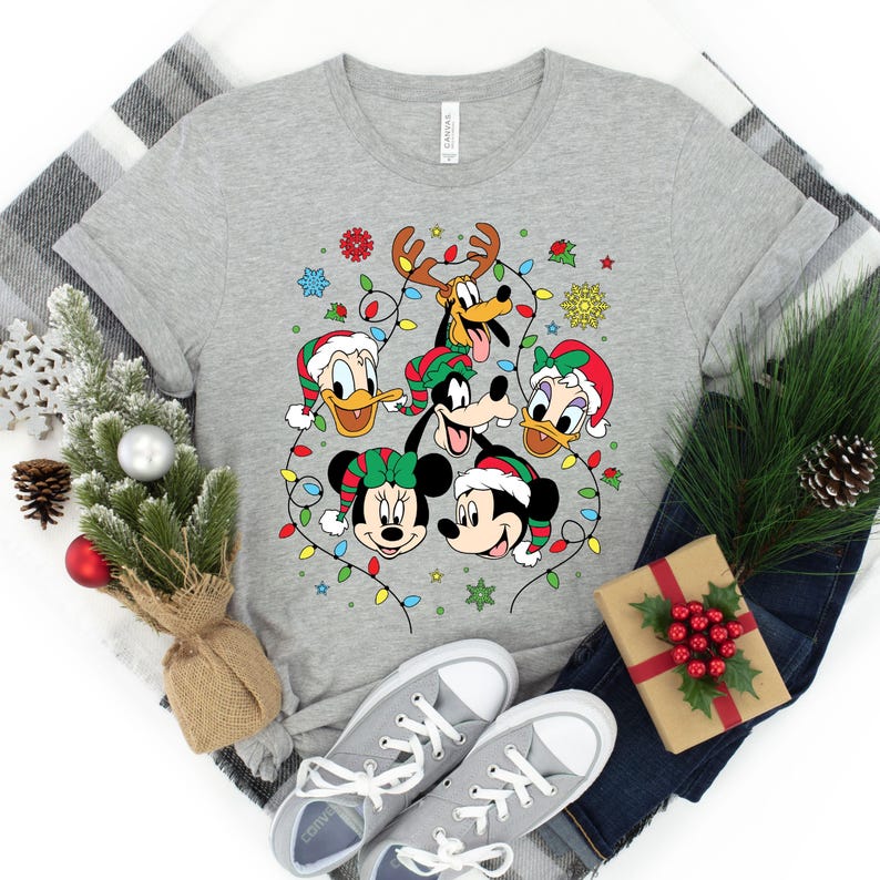 May include: A gray t-shirt with a Christmas-themed design featuring Mickey Mouse, Minnie Mouse, Donald Duck, Goofy, and Pluto. The characters are surrounded by colorful Christmas lights.