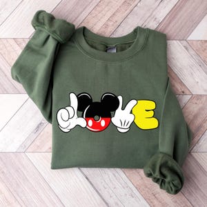 May include: Green sweatshirt with a Mickey Mouse design that spells out "LOVE". The "O" is Mickey's head and the "L" and "E" are Mickey's hands in the sign language for "love".