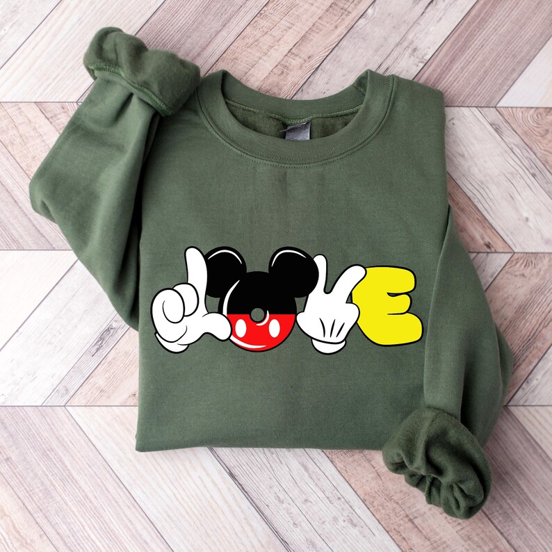 May include: Green sweatshirt with a Mickey Mouse design that spells out "LOVE". The "O" is Mickey's head and the "L" and "E" are Mickey's hands in the sign language for "love".