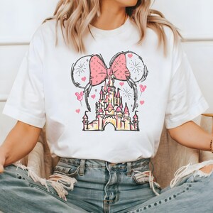 May include: White t-shirt with a pink bow and a cartoon drawing of a castle with fireworks and hearts.