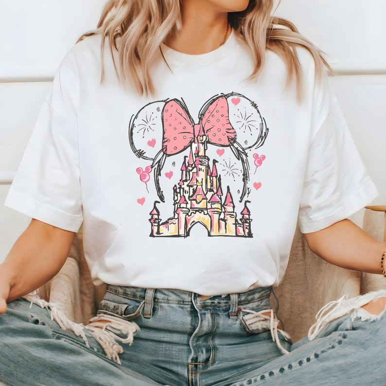 May include: White t-shirt with a pink bow and a cartoon drawing of a castle with fireworks and hearts.