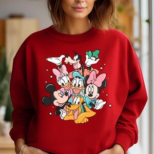 May include: Red sweatshirt with a graphic print of Mickey Mouse, Minnie Mouse, Donald Duck, Goofy, and Pluto. The characters are all smiling and appear to be hugging each other.