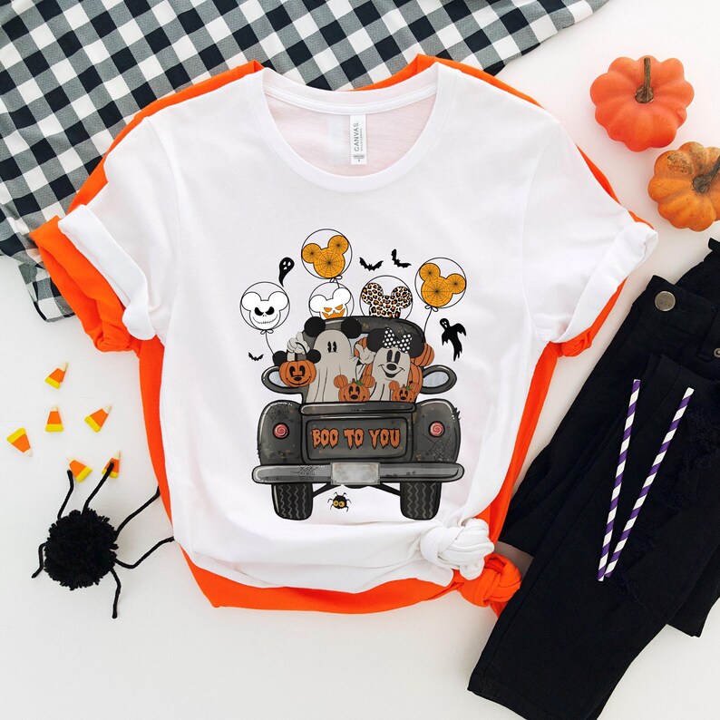 Peut inclure: T-shirt blanc avec un camion noir transportant Mickey Mouse et Minnie Mouse habill&eacute;s en costumes d'Halloween. Le camion porte l'inscription "Boo to You" &agrave; l'arri&egrave;re. Le camion est entour&eacute; de fant&ocirc;mes et de chauves-souris.
