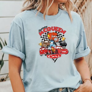 May include: Light blue t-shirt with a graphic of Lightning McQueen and other Cars characters. The graphic features the text "Lightning McQueen" and "Cars".