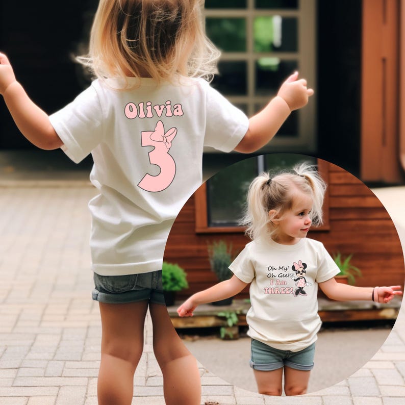 May include: White toddler t-shirt with the name "Olivia" and the number "3" in pink, with a bow graphic. The shirt is paired with denim shorts. A second image shows a toddler wearing a similar shirt with a Minnie Mouse graphic.