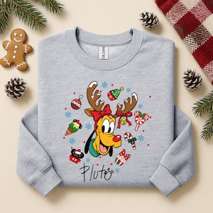 May include: A light gray sweatshirt featuring Pluto the dog with reindeer antlers and Christmas-themed decorations. The design includes a red bow, ornaments, and the word "Pluto" in script. Festive and seasonal.