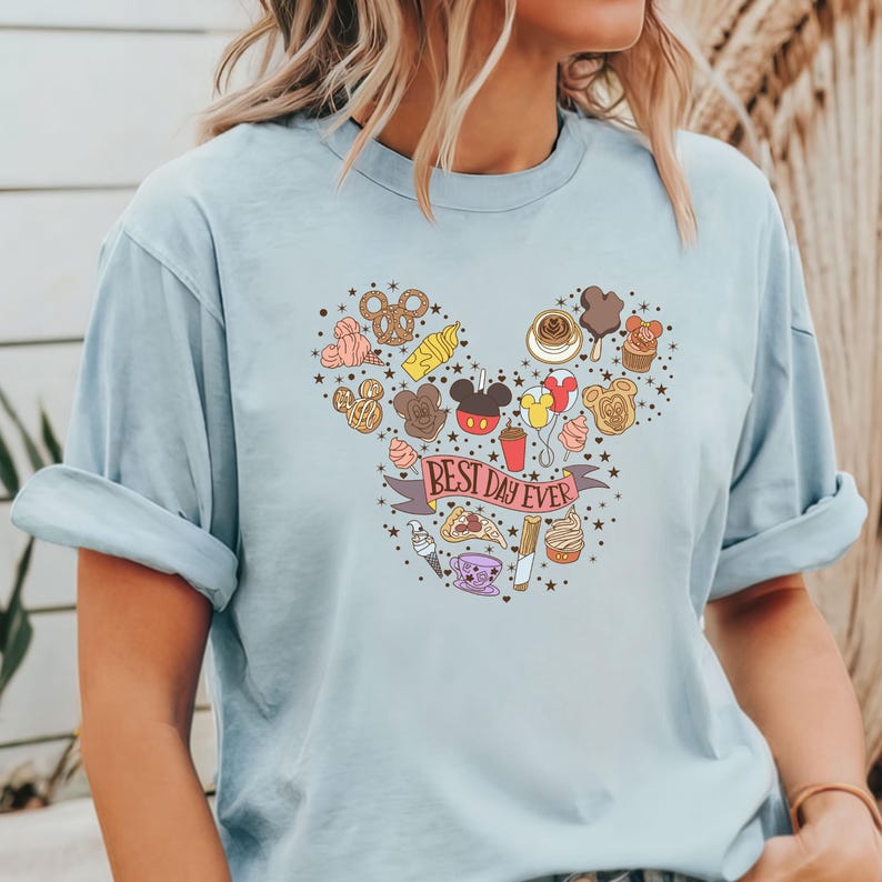 May include: Light blue t-shirt with a Mickey Mouse head design made up of various Disney food items. The text "Best Day Ever" is written on a banner.