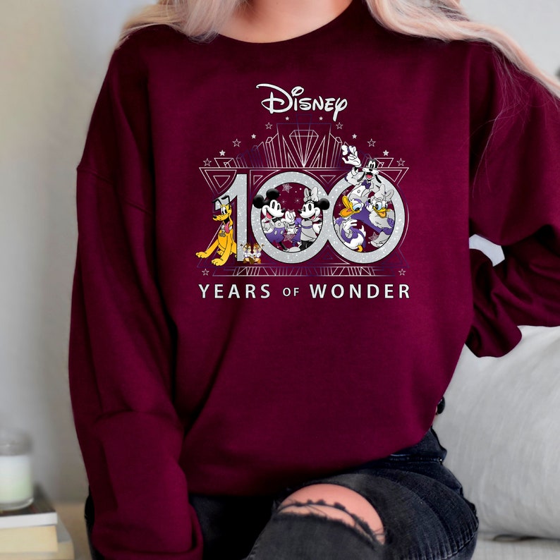 May include: Burgundy sweatshirt with a silver graphic of Mickey Mouse and friends celebrating Disney's 100th anniversary. The graphic includes the text "Disney" and "100 Years of Wonder".