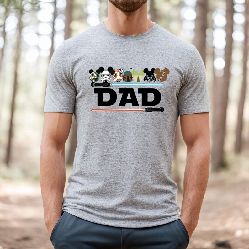 May include: Gray t-shirt with a graphic featuring cartoon character heads and the word "DAD" in black. A red lightsaber is below the text. The shirt has short sleeves and a crew neck.