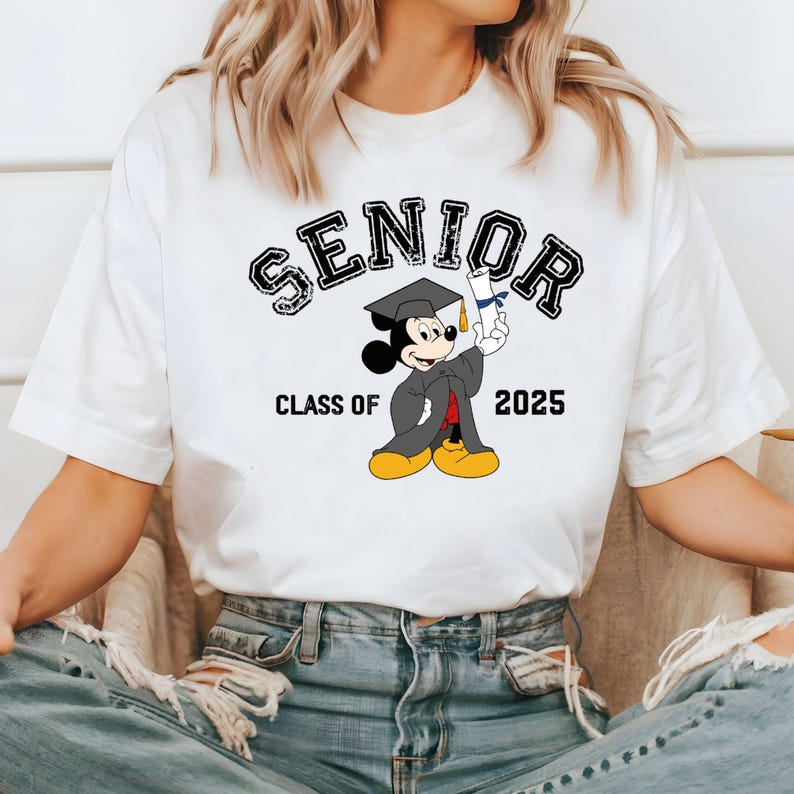 K&ouml;nnte beinhalten: Wei&szlig;es T-Shirt mit einer schwarzen Grafik von Mickey Mouse, der einen Abschluss-Hut tr&auml;gt und ein Diplom h&auml;lt. Der Text "SENIOR" befindet sich &uuml;ber Mickey Mouse und "CLASS OF 2025" darunter.