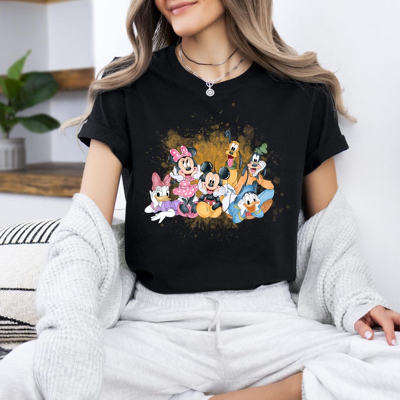 Puede incluir: Camiseta negra con un estampado gr&aacute;fico colorido de Mickey Mouse, Minnie Mouse, Donald Duck, Goofy y Pluto. Los personajes est&aacute;n rodeados de salpicaduras de pintura dorada.