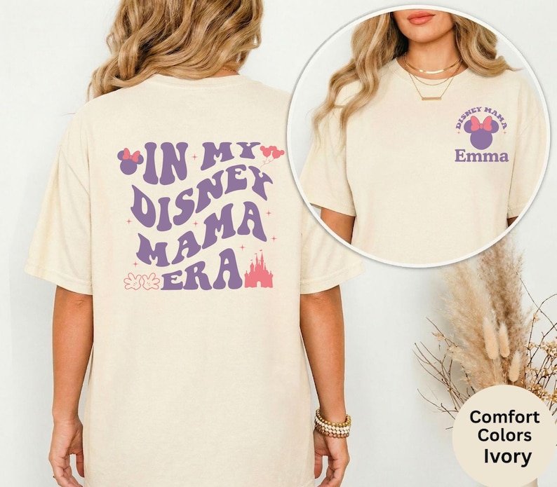 Puede incluir: Camiseta de color marfil con el texto "IN MY DISNEY MAMA ERA" en morado, con un lazo de Minnie Mouse y un castillo. La parte delantera de la camiseta tiene un gr&aacute;fico m&aacute;s peque&ntilde;o con el texto "DISNEY MAMA" y el nombre "Emma".