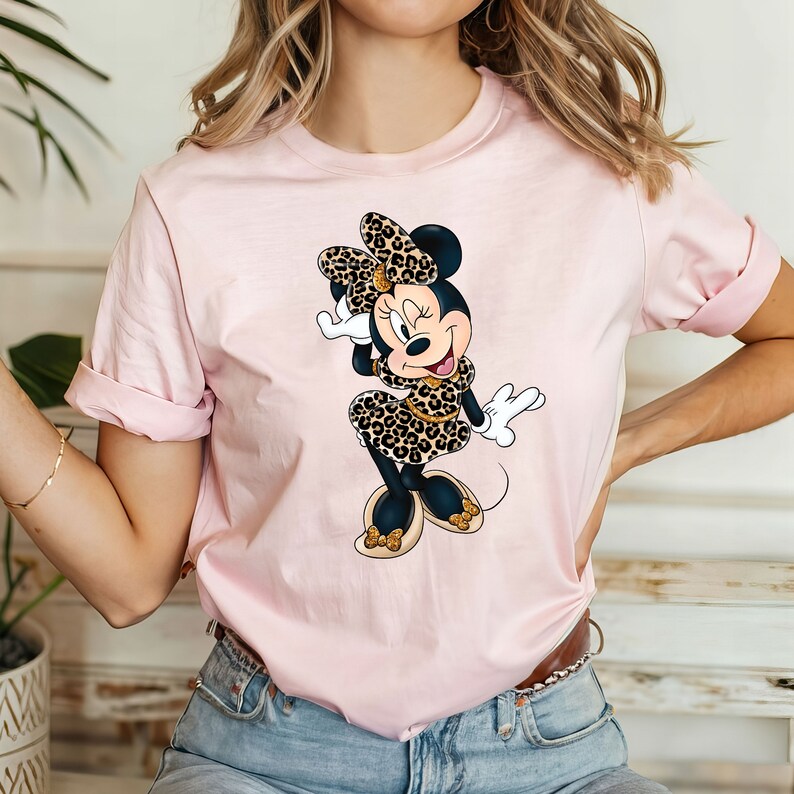 Op de afbeelding: Roze T-shirt met een cartoon afbeelding van Minnie Mouse die een luipaardprintjurk en een strik draagt.