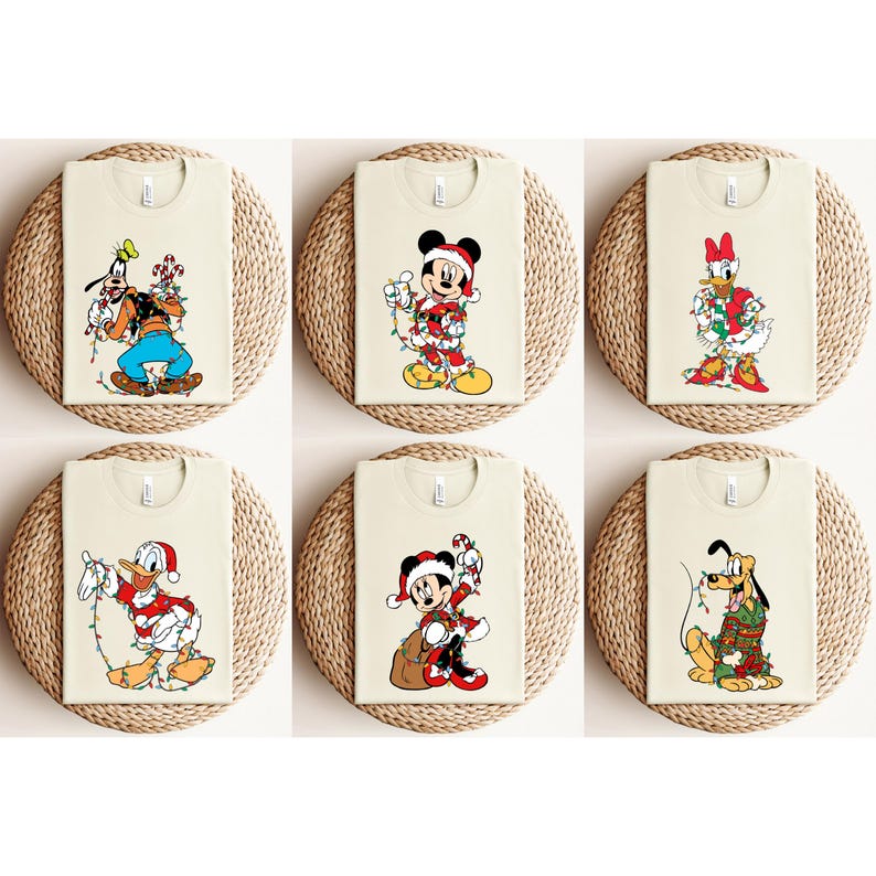 May include: Six cream-colored t-shirts featuring Disney characters in Christmas attire. Goofy, Mickey Mouse, Donald Duck, Minnie Mouse, and Pluto are shown with festive lights and Santa hats. Each shirt is displayed on a woven circular mat.