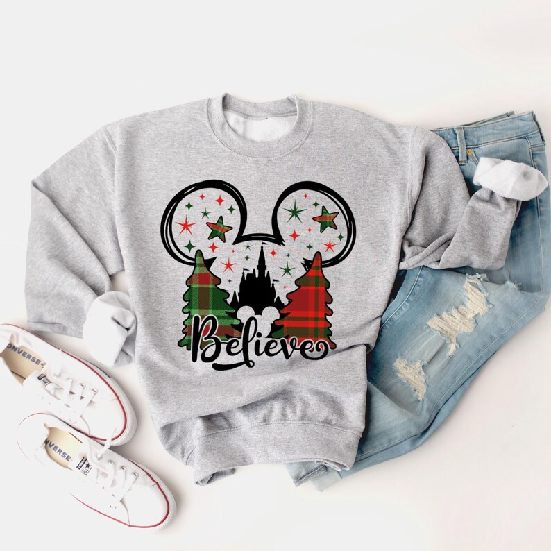 Puede incluir: Sudadera gris con un dise&ntilde;o de Mickey Mouse en cuadros rojos y verdes con un castillo y estrellas. El texto "Believe" est&aacute; impreso debajo del dise&ntilde;o.