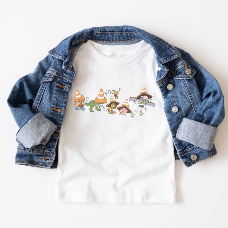 Op de afbeelding: Wit T-shirt met een afbeelding van Toy Story-personages die verkeerskegels dragen. De personages zijn Woody, Buzz Lightyear, Rex, Hamm en Slinky Dog.