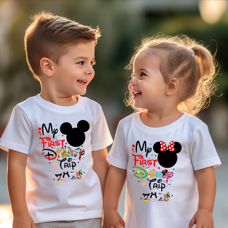 Peut inclure: Deux enfants portant des t-shirts blancs avec l'inscription "My First Disney Trip 2023". Les chemises pr&eacute;sentent une t&ecirc;te de Mickey Mouse noire et une t&ecirc;te de Minnie Mouse avec un n&oelig;ud rouge. Le texte est multicolore.