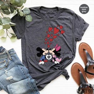 May include: A heather dark grey t-shirt with a graphic of Mickey Mouse and Minnie Mouse kissing.  The graphic is surrounded by red hearts.