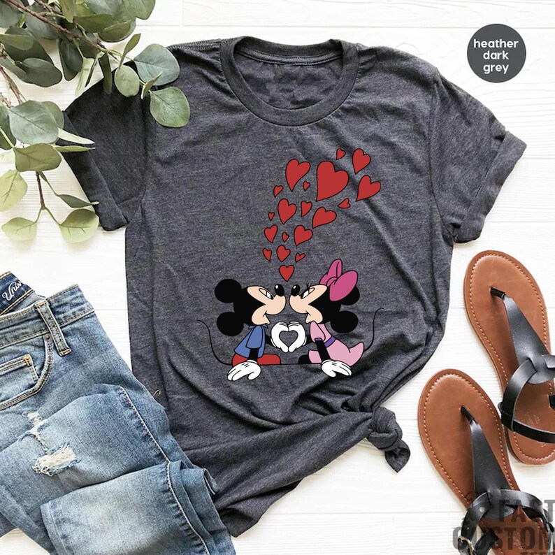 May include: A heather dark grey t-shirt with a graphic of Mickey Mouse and Minnie Mouse kissing.  The graphic is surrounded by red hearts.