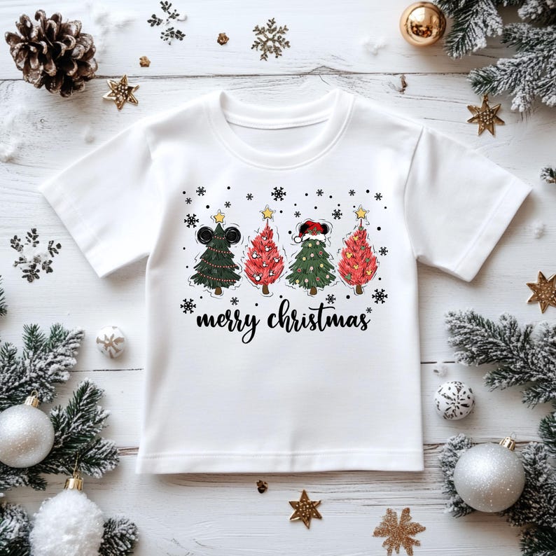 May include: White t-shirt featuring four Christmas trees with mouse ears, decorated with stars and snowflakes. The text "merry christmas" is written in a script font below the trees. Festive holiday apparel.