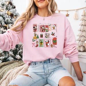 May include: A light pink sweatshirt featuring a festive Christmas design with cartoon characters and the words "Merry Christmas." The design includes Mickey Mouse, Minnie Mouse, Donald Duck, and other holiday elements.